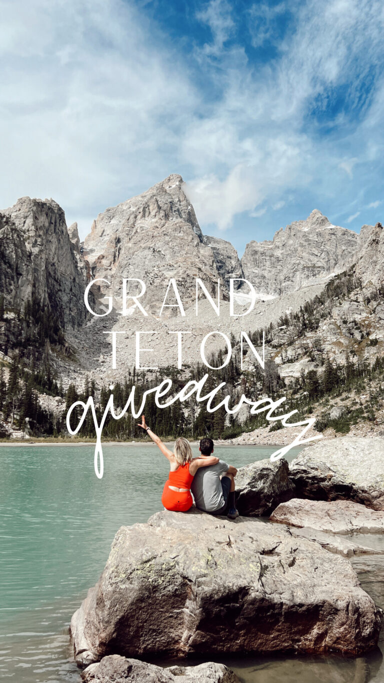 Kam and husband sitting on rocks at turquoise alpine lake with Grand Teton mountains behind them