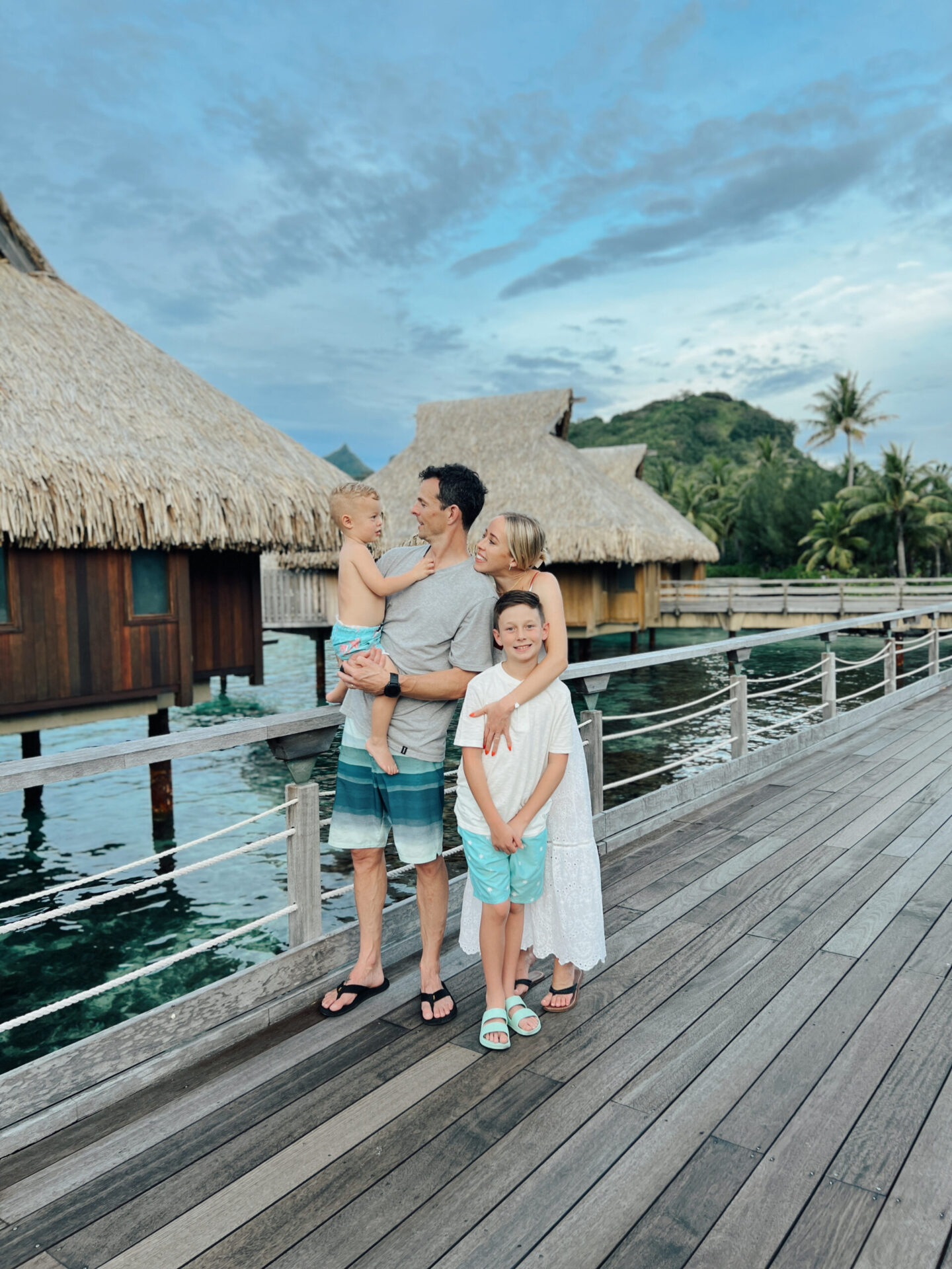 Kam with two sons standing on wooden deck between overwater bungalows at tropical resort