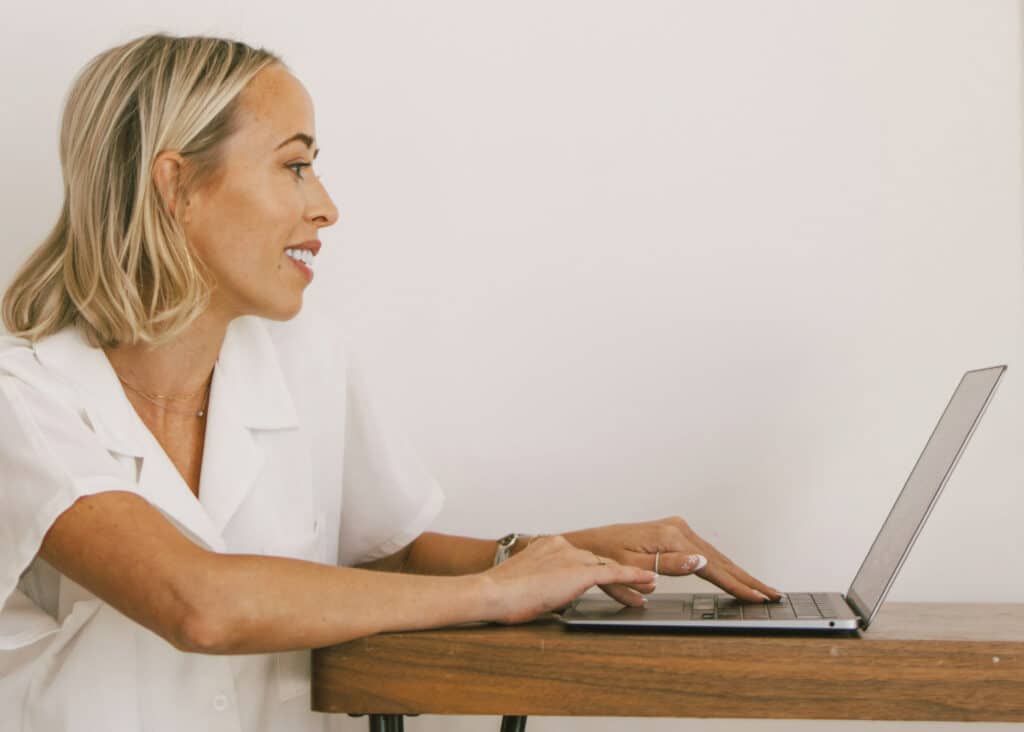 Professional travel consultant smiling while working on a laptop  representing the expert family travel coaching services of Our Family Passport.